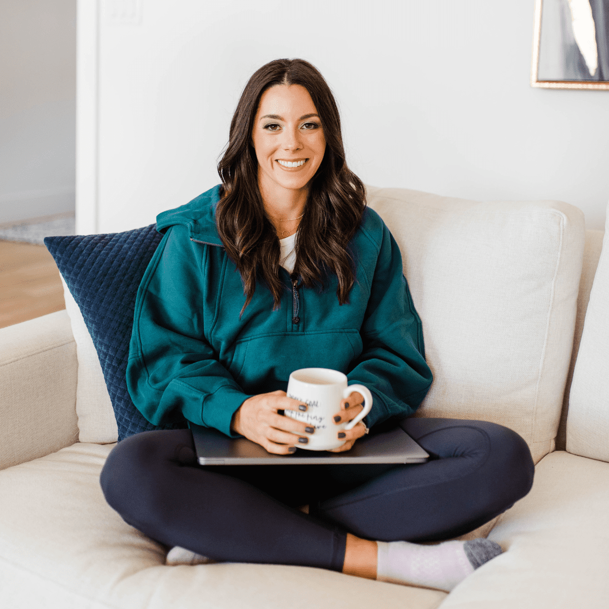 Kacie Barnes sitting on a couch holding her laptop and coffee mug.