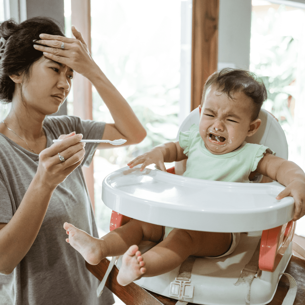Frusted mom feeding crying toddler in high chair