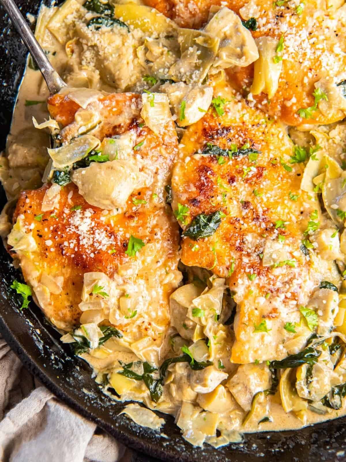 partial view of spinach artichoke chicken in a cast iron skillet.