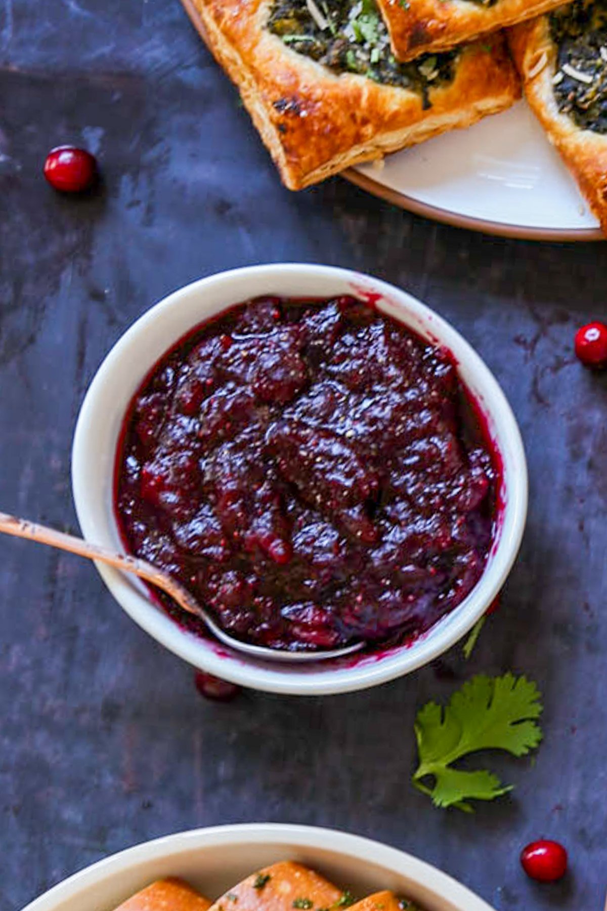 bowl of cranberry chutney as part of a Thanksgiving spread, text overlay