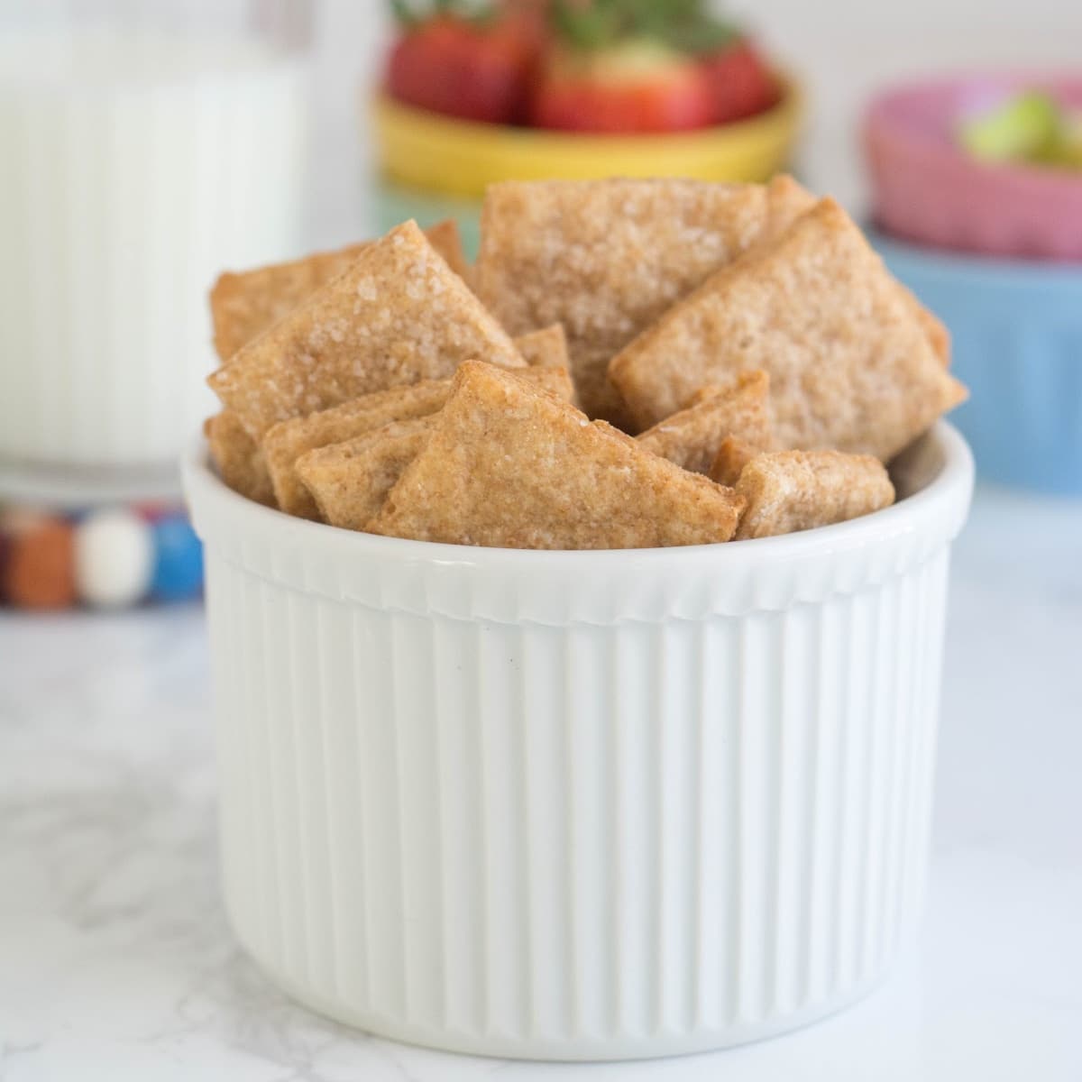 A small white ramekin filled with homemade crackers sits on a white countertop.